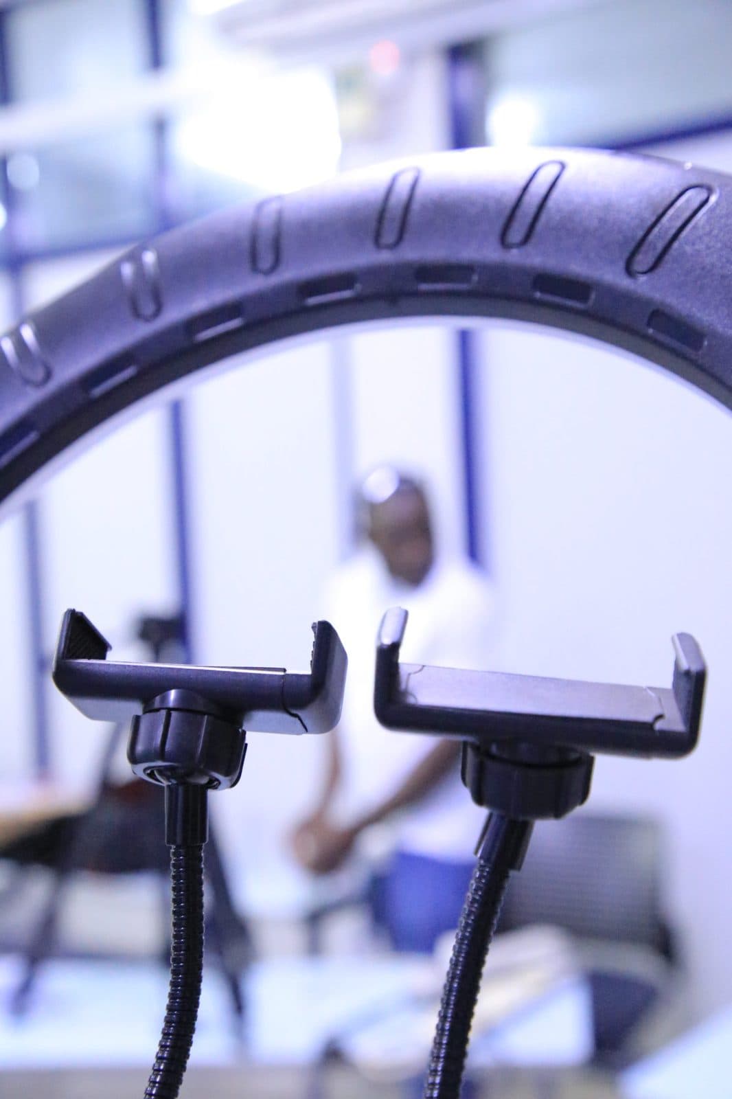 Phone holders on a ring light in sharp focus, a crew member blurred behind