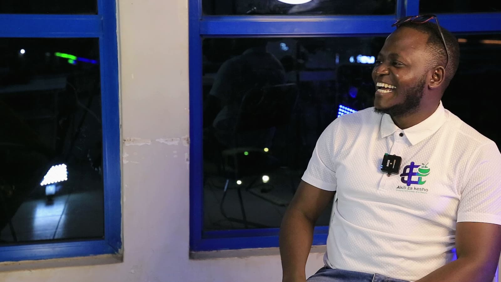 Laughing on set at night in an Akili za Kesho shirt